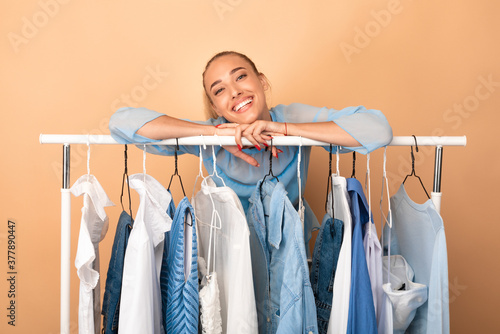 Portrait of cheerful woman leaning on rack with clothes