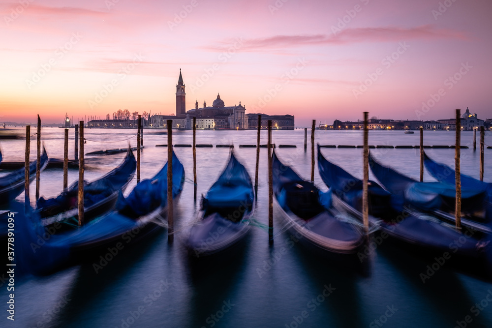 Docked gondolas in the Laguna Veneta with the Bazilika San Giorgio Maggiore in the background during the sunrise in Venice, Italy