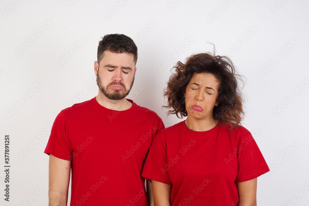 Dismal gloomy rejected Young beautiful couple wearing red t-shirt on white has problems and difficulties, curves lower lip and closes eyes in despair, being in depression after desperate attempts Dismal gloomy rejected Young beautiful couple wearing red t-shirt on white has problems and difficulties, curves lower lip and closes eyes in despair, being in depression after desperate attempts