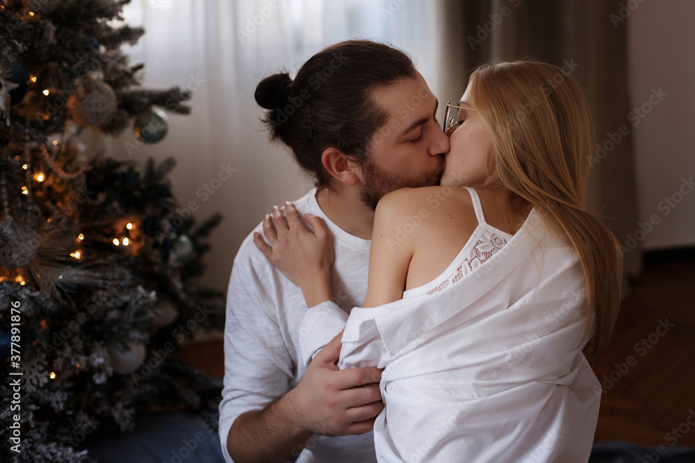 Girl and boyfriend kissing in apartment in the background of the Christmas tree on Christmas Day