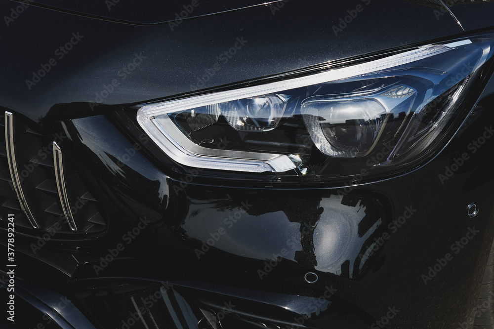 Black luxury sports car closeup. Modern LED headlights with lenses. Aggressive design. Car showroom. Closeup. 