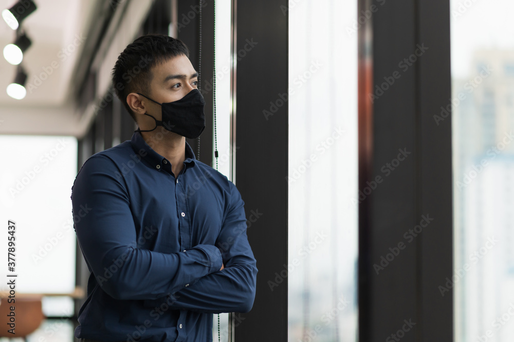 Business asian man wearing protection face mask standing near window in office. Business asian man wearing protection face mask standing near window in office.