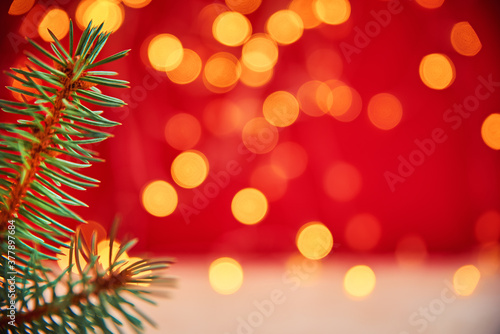 Christmas background. Fir tree branch against blured bokeh lights on a red background