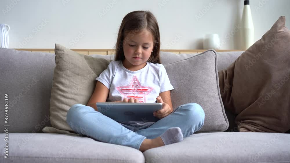 Pretty girl drawing with forefinger on digital tablet. Happy female kid using modern device at home. Concept of creativity and activity. Pretty girl drawing with forefinger on digital tablet. Happy female kid using modern device at home. Concept of creativity and activity.