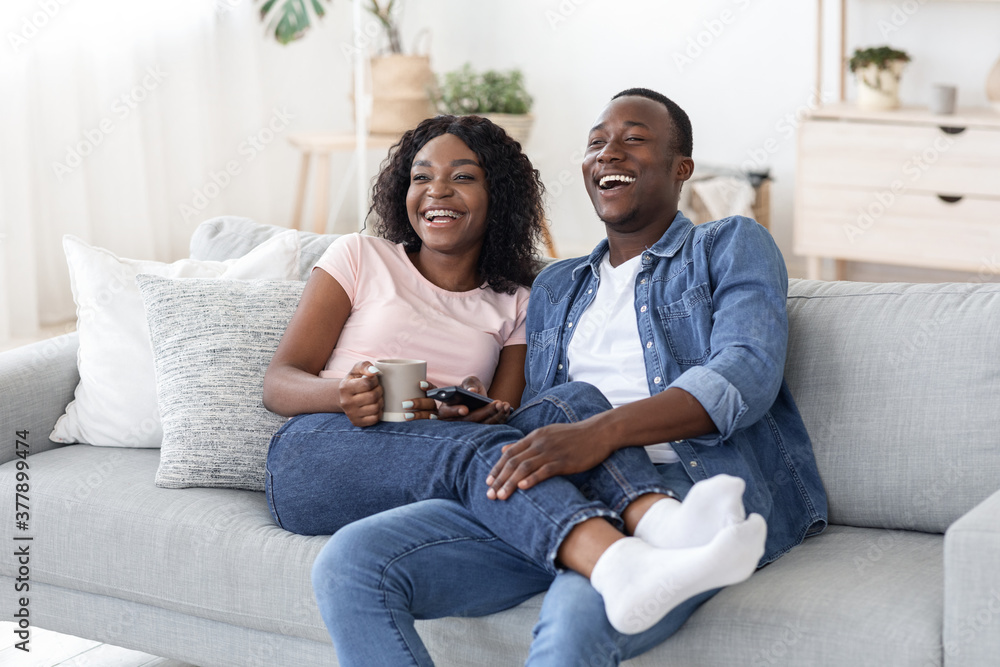 Joyful african man and woman drinking tea and watching movie