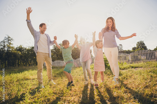 Evening sunset sky summer picnic relax concept. Full size photo of positive family mom dad little kids hold hands enjoy weekend in green grass outside city park garden