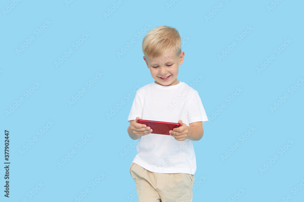 Cute smilling child boy with smartphone on blue background. Advertising of educational applications on a mobile phone for children. Funny face. Cute smilling child boy with smartphone on blue background. Advertising of educational applications on a mobile phone for children. Funny face.