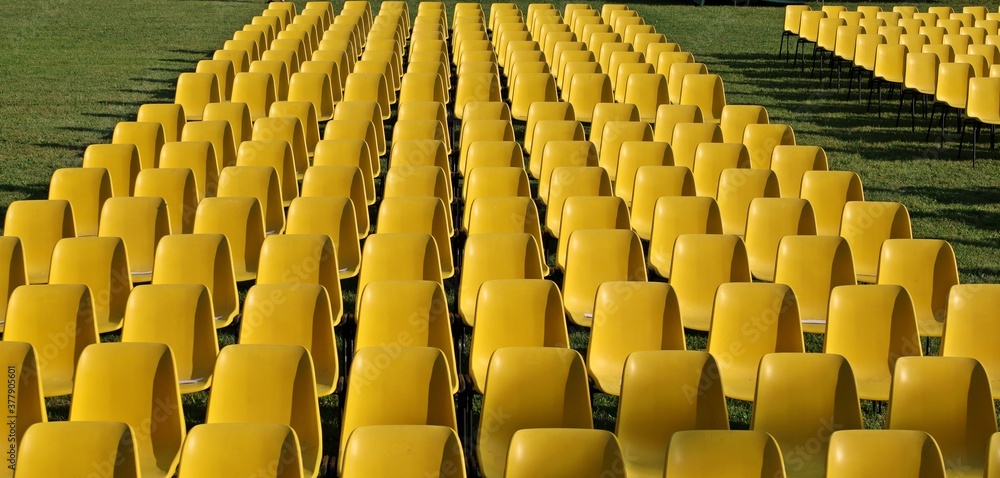 Fototapeta premium Long rows of empty yellow plastic chairs geometrically arranged on a lawn. Texture and background. Copy space..