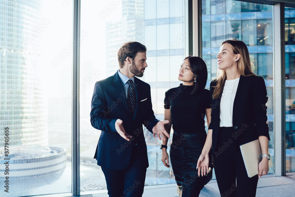 Prosperous male boss in formal wear walking in office interior with female administrative assistance discussing working process, group of woman and man colleagues talking to each other about business Prosperous male boss in formal wear walking in office interior with female administrative assistance discussing working process, group of woman and man colleagues talking to each other about business