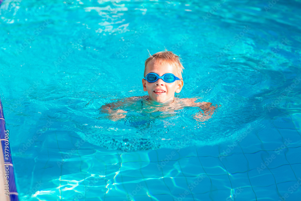 Cute happy little boy in goggles swimming in the swimming pool