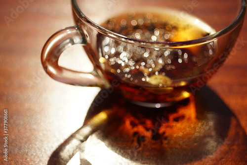 Glass cup with black tea on the sunny brown table. Closeup view with amazing light and shadow