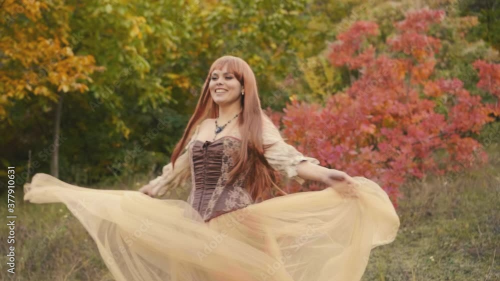 Happy, joyful beautiful young woman in a medieval dress is dancing, spinning in the autumn forest and enjoying the wild nature. Creative clothing, brown medieval royal vintage dress. Long red hair Happy, joyful beautiful young woman in a medieval dress is dancing, spinning in the autumn forest and enjoying the wild nature. Creative clothing, brown medieval royal vintage dress. Long red hair