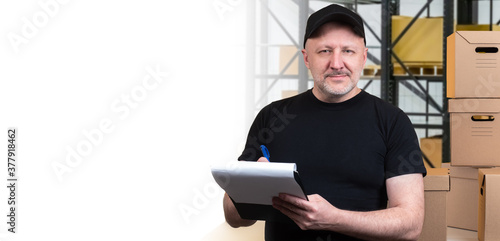 The concept of storage. A storekeeper with a folder in his hands looks at the camera. A friendly man fulfills orders in the warehouse. Space for text. Man on the background of shelves with boxes. photo