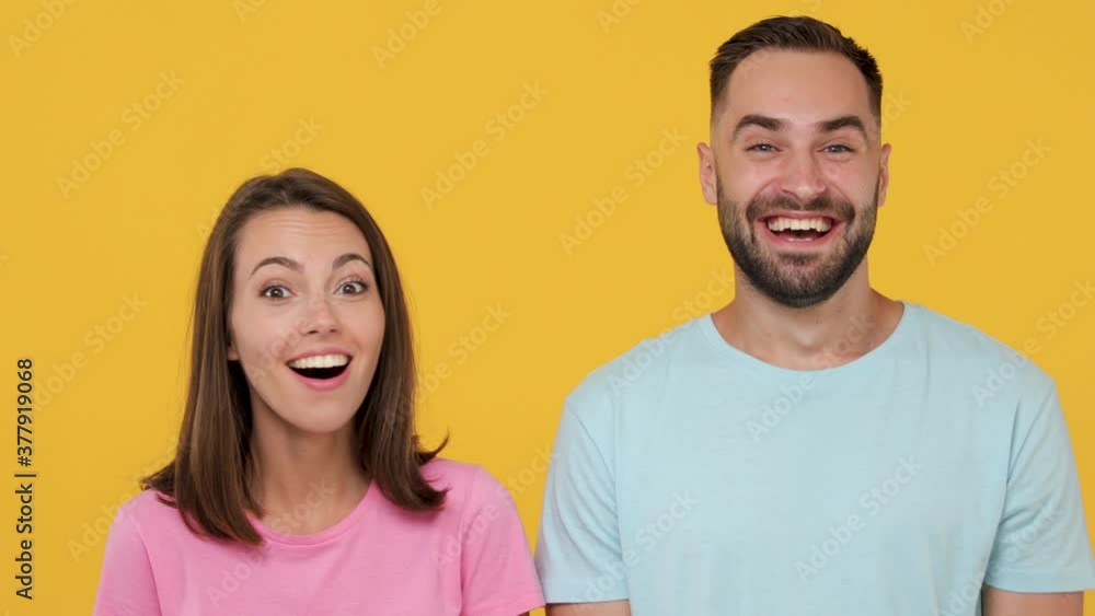 Close up young couple friends bearded man woman 20s in basic t-shirts posing isolated on yellow background studio. People emotions lifestyle concept. Look at camera surprised and to each other say wow Close up young couple friends bearded man woman 20s in basic t-shirts posing isolated on yellow background studio. People emotions lifestyle concept. Look at camera surprised and to each other say wow