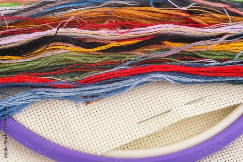 Colorful cross stitch embroidery threads with needle on a canvas.