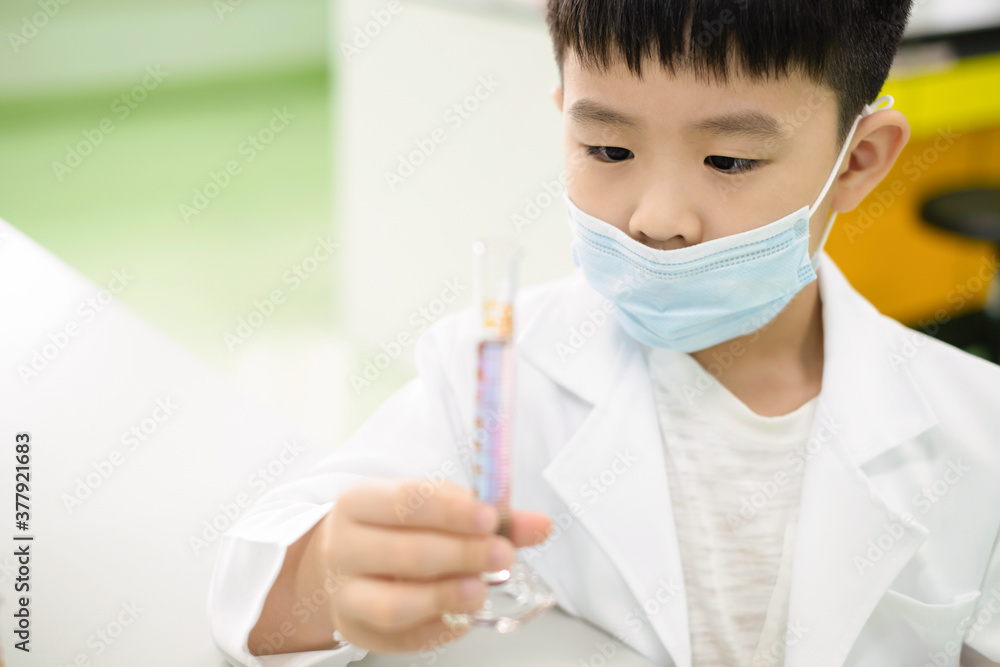 Elementary school student doing a science experiment. A boy looking at purple solution in a cylinder and feeling happy and fun on the mixing of the solution. Experiment concept. Elementary school student doing a science experiment. A boy looking at purple solution in a cylinder and feeling happy and fun on the mixing of the solution. Experiment concept.