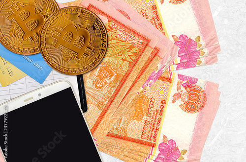 100 Sri Lankan rupees bills and golden bitcoins with smartphone and credit cards. Cryptocurrency investment concept. Crypto mining or trading photo