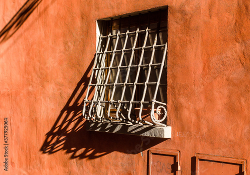 Old iron grating window on a red plaster wall in typical italian alley