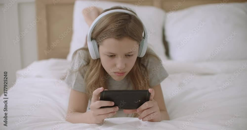 teen girl is surfing internet on smartphone, reading information from site, lying on bed in home after school teen girl is surfing internet on smartphone, reading information from site, lying on bed in home after school