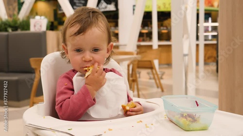 Cute funny little baby child girl eating unsavory meat spit it out from mouth in a mall food court photo