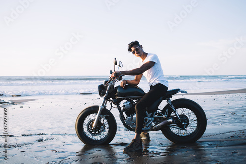 Young male sitting on motorcycle on beach