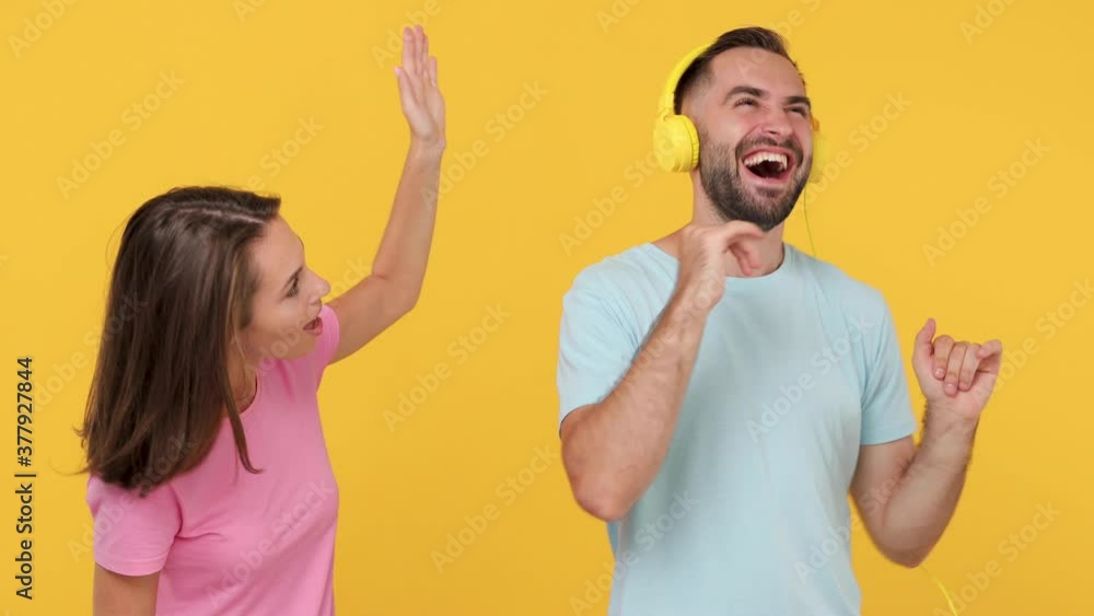 Young couple friends bearded woman man 20s in basic t-shirts posing isolated on yellow background studio. Dancing fooling around having fun expressive gesticulating hands listen music in headphones Young couple friends bearded woman man 20s in basic t-shirts posing isolated on yellow background studio. Dancing fooling around having fun expressive gesticulating hands listen music in headphones
