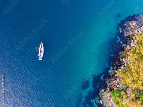 Aerial drone bird's eye view of one sailboat yacht anchored at Store Beach near Quarantine Station in Manly, the beachside suburb of Sydney, New South Wales, Australia, in the evening before sunset.