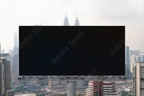 Blank black road billboard with Kuala Lumpur cityscape background at day time. Street advertising poster, mock up, 3D rendering. Front view. Concept of marketing to promote or sell services or ideas.