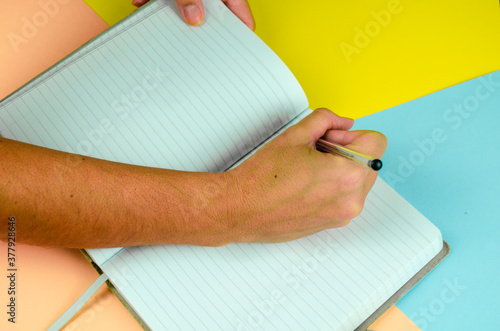 mano tomando notas en una libreta con fondo liso de colores