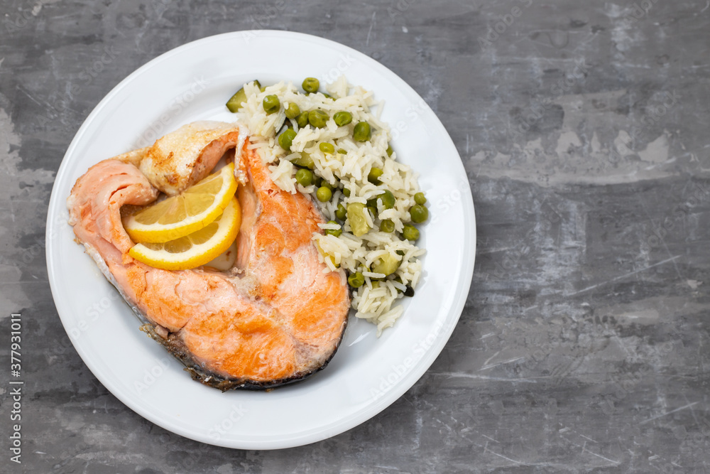 fried salmon with rice with vegetables on white plate on ceramic background