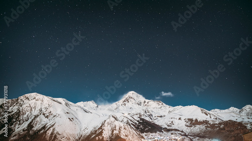 Georgia. Winter Night Starry Sky With Glowing Stars Over Peak Of Mount Kazbek Covered With Snow. Beautiful Night Georgian Winter Landscape