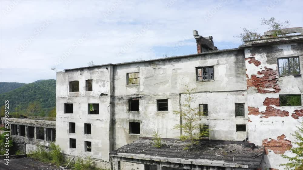 Aerial view of exterior of an old destroyed ore dressing and mineral dressing factory at Far East of Russia. Trees grow on its roof. Green hills are on the background Aerial view of exterior of an old destroyed ore dressing and mineral dressing factory at Far East of Russia. Trees grow on its roof. Green hills are on the background