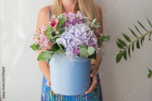 Flower arrangement in a blue hat box was created by a florist for a wedding gift. Flower bouquet of purple hydrangea, pink calla, pink reses, eustoma flowers and eucalyptus in womens hands