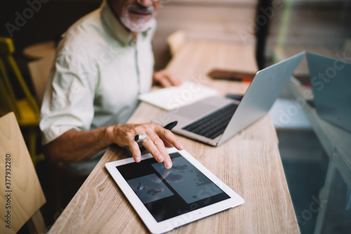 Crop senior man browsing tablet in creative workplace