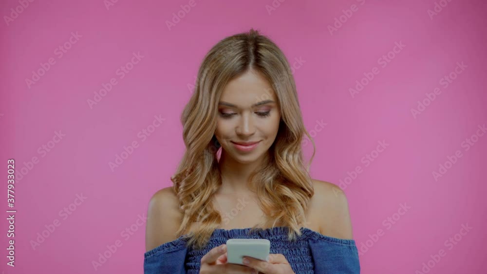 Blonde woman using smartphone and looking at camera isolated on purple Blonde woman using smartphone and looking at camera isolated on purple