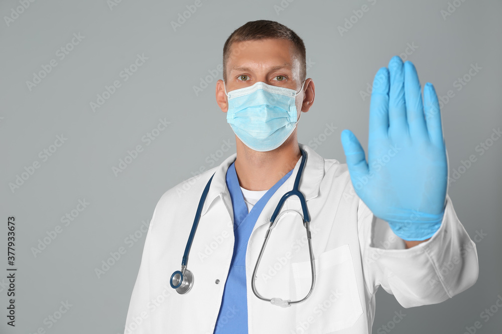 Doctor in protective mask showing stop gesture on grey background. Prevent spreading of coronavirus Doctor in protective mask showing stop gesture on grey background. Prevent spreading of coronavirus