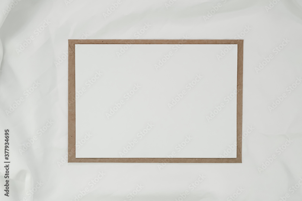 Blank white paper on brown paper envelope with white cloth. Mock-up of horizontal blank greeting card. Top view of Craft envelope on white background. Flat lay minimalism Blank white paper on brown paper envelope with white cloth. Mock-up of horizontal blank greeting card. Top view of Craft envelope on white background. Flat lay minimalism