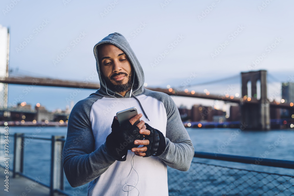 African American young guy listening to music and texting on smartphone
