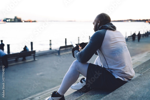 Black man with smartphone sitting on step before embankment
