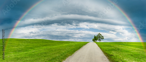 Landstrasse in grüner hügeliger Landschaft mit Regenbogen