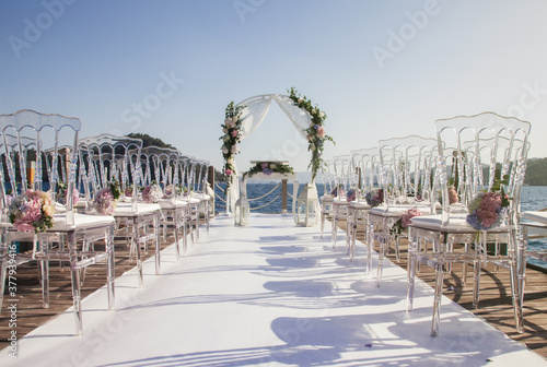 Magnificent design of wedding ceremony on coast of azure sea. Arch for newlyweds marriage registration in modern style. Venue of luxury wedding with amazing landscape. Copyright space for site © Alex Vog