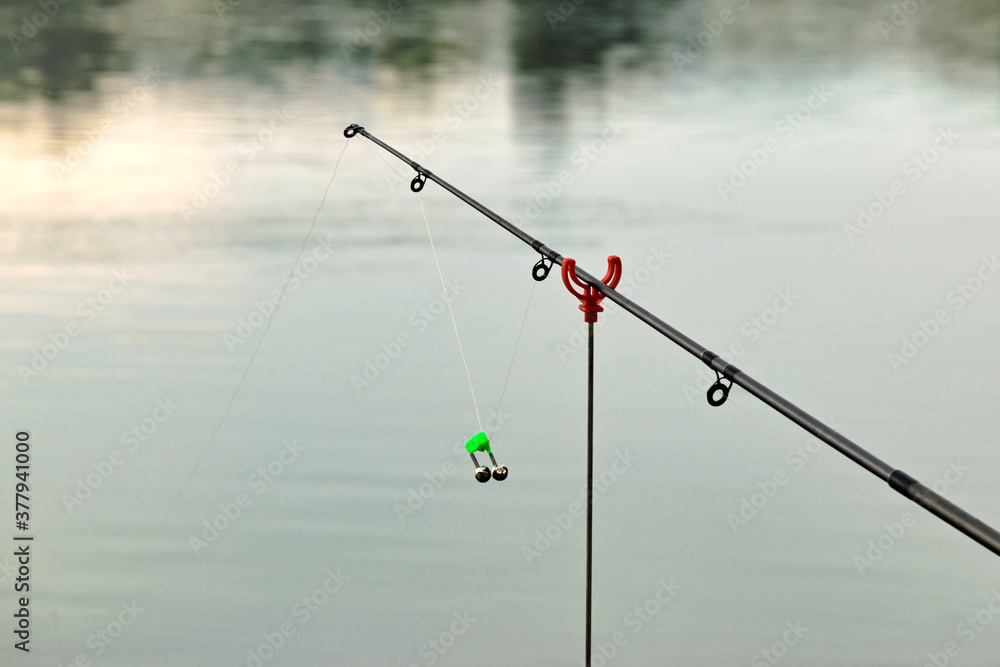 Fishing rod bell on fishing line, lake at sunset background