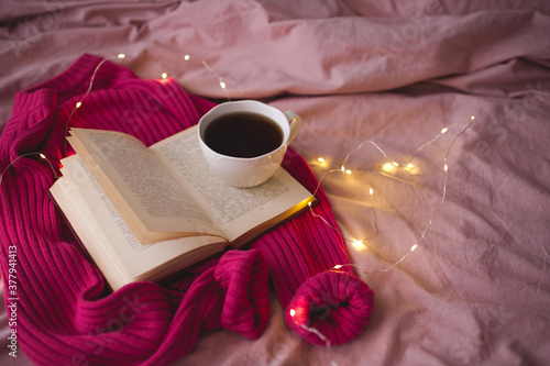 Tasty cup of tea with knitte cloth and open book in bed. Good morning. Selective focus.