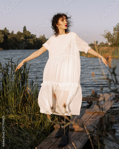 
A girl in a solid dress and black boots stands by the river