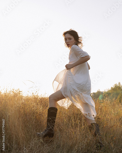 
A girl in a white dress walks across the field at sunset