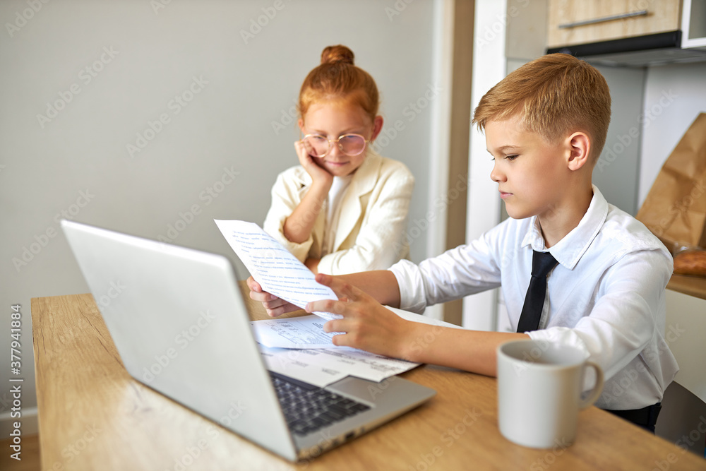 friendly kids couple behave themselves as adults, solve work problems together, look at laptop and documents, checking bills, making purchase online, freelance. children, people concept friendly kids couple behave themselves as adults, solve work problems together, look at laptop and documents, checking bills, making purchase online, freelance. children, people concept