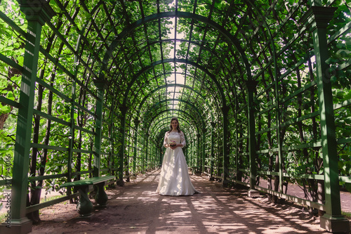 Bride with wedding bouquet in hands on background of green leaves in the Park. Pretty woman in wedding dresses on Sunny wedding day. Female in amazing view. Happy bride on background green