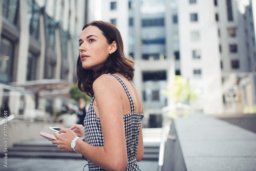Adult worried woman looking away while using smartphone on street in downtown