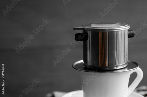 White cup of coffee with a metal filter on a top and scattered beans on a wooden table. Traditional vietnamese coffee.