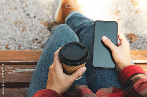 Woman in jeans and shirt hold paper cup and phone outdoor